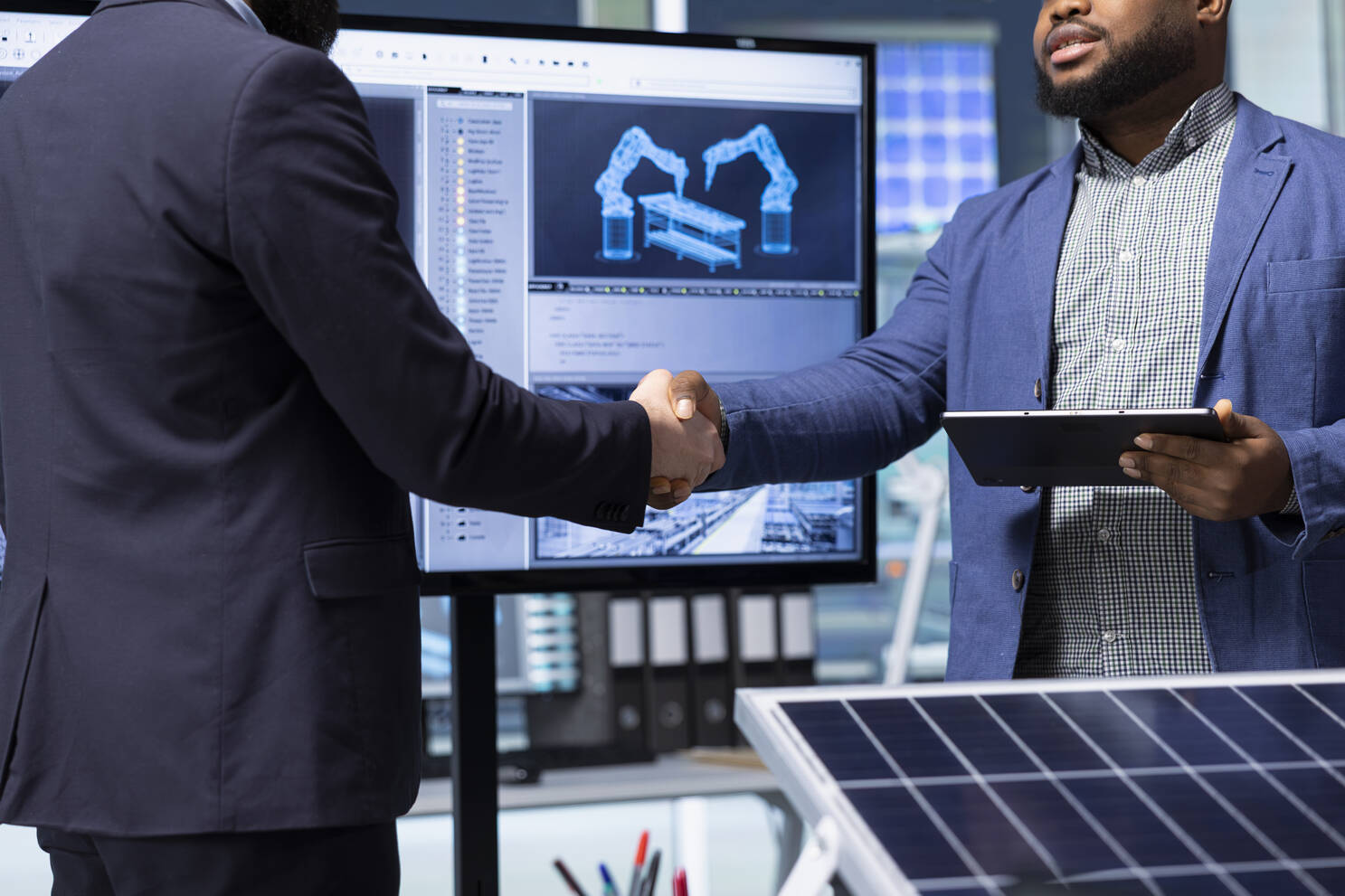 Two businessmen shaking hands in an office arm design on screen and enrgy panel in foreground